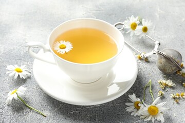 Tasty chamomile tea, infuser and flowers on light grey table, closeup