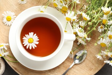 Tasty chamomile tea and flowers on black table, flat lay