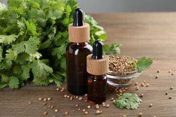 Aromatic oil in bottles, cilantro leaves and coriander seeds on wooden table, closeup