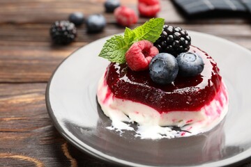 Delicious panna cotta with berries, jam and mint on wooden table, closeup