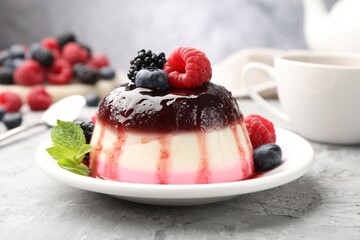 Tasty panna cotta with berries and jam on light grey table, closeup