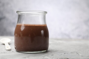 Delicious panna cotta in glass jar on grey textured table, closeup. Space for text