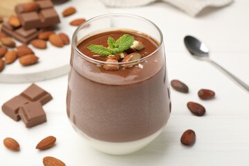 Delicious chocolate panna cotta with almonds, mint and cocoa beans on white wooden table, closeup