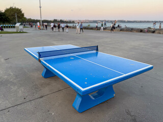 Bright blue table tennis table situated at a seaside promenade during a pleasant evening with...
