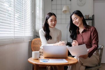 Two businesswomen collaborating on project using laptop and documents in modern office