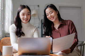 Two businesswomen collaborating on laptop with documents in modern office