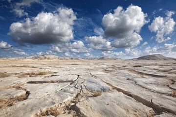 Dry, cracked earth landscape under a vast blue sky with puffy white clouds