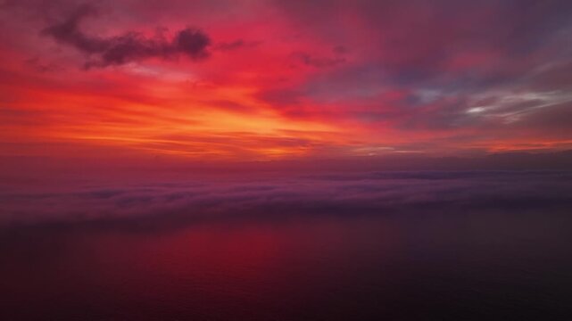 Aerial view of warm sunset hues reflecting off the tranquil waters, contrasting with the soft, rolling clouds below, Cape Town, Western Cape, South Africa.