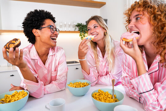 Multiethnic group of young female friends having breakfast during pajamas party - Powered by Adobe