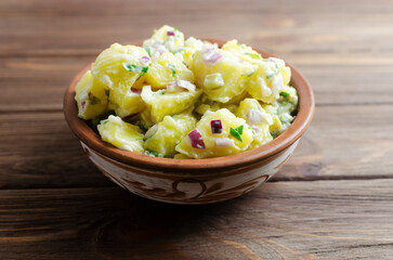 Cold potato salad with purple onion, gherkins and parsley in a ceramic bowl on a wooden table....