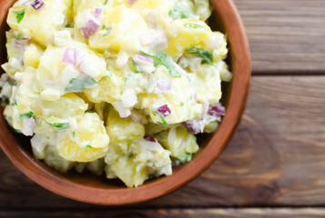 Cold potato salad with purple onion, gherkins and parsley in a ceramic bowl. Traditional German dish concept. Rustic style. Selective focus. Horizontal orientation. copy space. Top view
