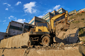Excavator stands on the ruins of a factory. Process of dismantling, demolition