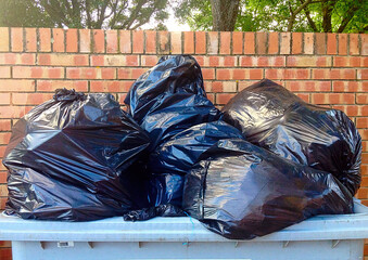 Overflowing garbage bin with black plastic bags near brick wall
