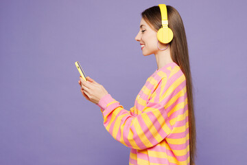 Side view young woman she wear yellow sweatshirt casual clothes listen to music in headphones use...