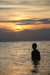Silhouette of a man standing in shallow ocean water during a golden sunset, perfect for travel and lifestyle photography