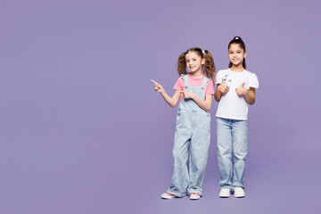 Fototapeta premium Full body fun little two friends kids children girls 9-10 years old wear casual clothes together point index finger aside on area show thumb up isolated on plain purple background. Lifestyle concept.