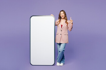 Full body young woman wear beige jacket formal clothes big huge blank screen mobile cell phone smartphone with area point finger up isolated on plain pastel light purple background. Lifestyle concept.