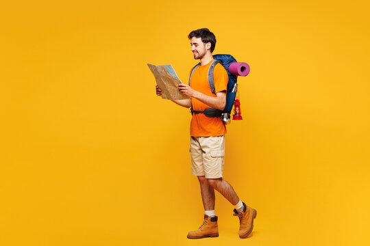 Full body young traveler man carry backpack with stuff mat read paper map isolated on plain yellow background Tourist leading active lifestyle walk on spare time Hiking trek rest travel trip concept. - Powered by Adobe