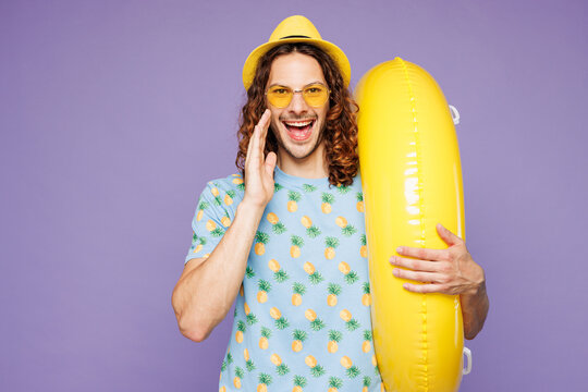 Young man wear blue beach t-shirt yellow hat sunglasses rest near hotel pool hold rubber ring scream hold put hand near mouth isolated on plain purple background. Summer vacation sea sun tan concept.