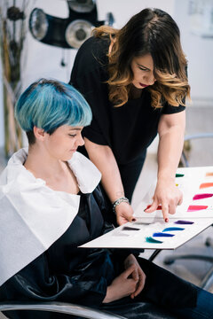 A professional hairstylist assists her female client in selecting a new hair color. They are reviewing a wide range of vibrant color swatches together at a modern hair salon.