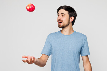 Young smiling happy cheerful man wear blue t-shirt casual clothes hold in hand eat toss up red...