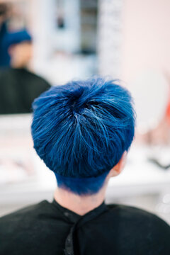 A person with vibrant blue hair is seen from behind in a salon setting. This unique hairstyle showcases individuality and modern hair trends, reflecting a bold personal statement.