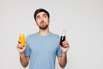 Young minded man wear blue casual clothes hold bottles of smoothie orange green juice and cola...