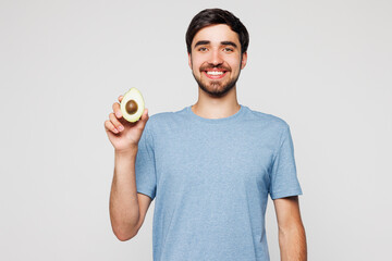 Young smiling happy fun man wear blue t-shirt casual clothes hold in hand half of avocado look...