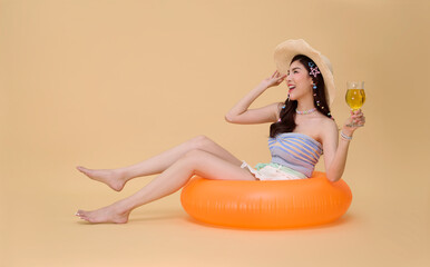 Summer vacation travel woman relaxing on orange inflatable ring holding cocktail on beige studio...