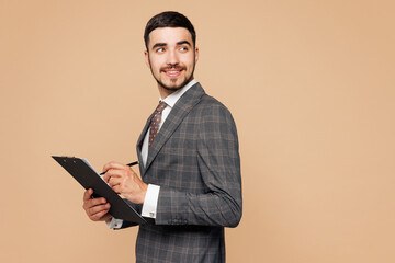 Side view young employee business man corporate lawyer he wearing grey suit shirt tie work in office hold clipboard with paper account documents look aside isolated on plain beige background studio.