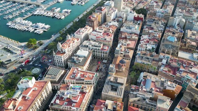 Aerial view of the marina with many boats and buildings with red rooftops, creating a vibrant cityscape from above, Alicante, Valencian Community, Spain.