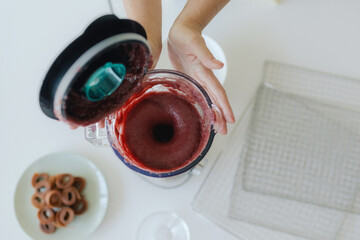 Closeup of a woman’s hands preparing a smoothie in a blender with fresh fruit for a healthy...