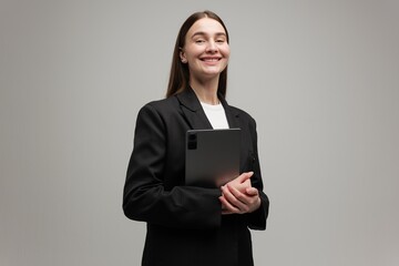 Confident businesswoman in formal attire holding a tablet while smiling brightly in a minimalist...