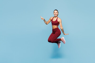 Obraz premium Full body young fitness trainer instructor woman sportsman wearing red sportswear train in home gym jump high point index finger aside isolated on plain blue background. Workout sport fit abs concept.
