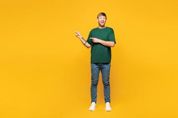 Fototapeta premium Full body young smiling happy man wear green t-shirt casual clothes point index finger aside on blank empty area mock up isolated on plain yellow orange background studio portrait. Lifestyle concept.