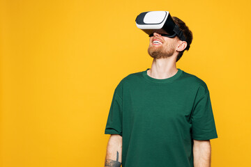 Young excited fun happy Caucasian man he wearing green t-shirt casual clothes watching in vr headset pc gadget play game isolated on plain yellow orange background studio portrait. Lifestyle concept.