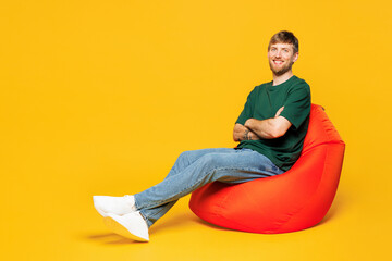 Full body young smiling happy man wear green t-shirt casual clothes sit in bag chair hold hands...