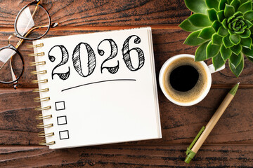 New year resolutions 2026 on desk. 2026 goals list with notebook, coffee cup, plant on wooden...