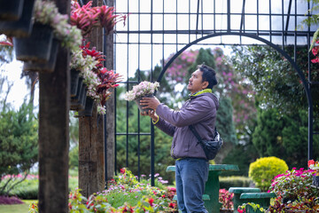 Young Asian gardener is choosing flowering plant from the local garden center nursery full of...