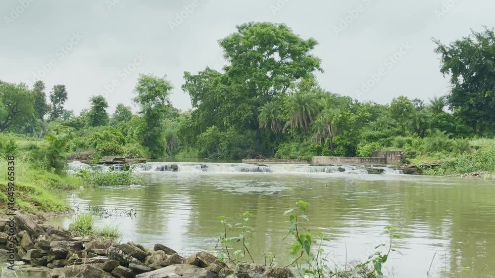 Poster static shot of a serene natural landscape featuring a calm river or stream flowing through a lush, g