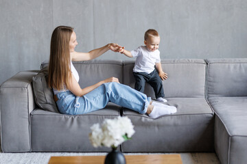 Adorable toddler son play sitting on sofa next to him during play