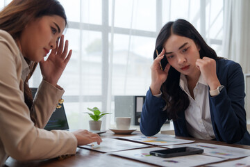 Two businesswomen feeling stressed while analyzing financial reports in office