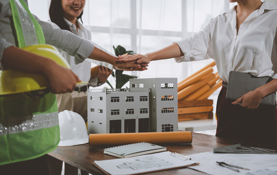 Architects joining hands over building model, teamwork and collaboration in architectural design