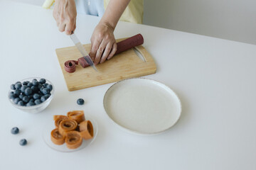 Caucasian woman preparing homemade fruit leather, slicing fresh fruit in her kitchen for a healthy...