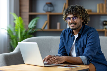 A cheerful individual actively working on their laptop with a welcoming smile, seated in a cozy and...