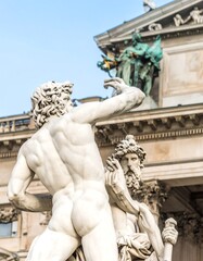 Fototapeta premium Rear view of two large, muscular, marble statues, one nude, the other draped, against a classical building
