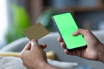 Close-up of a person holding a smartphone with a green screen and a credit card, implying online payment, e-commerce, or digital transaction concepts in a modern lifestyle setting.