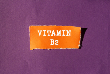 Vitamin B2 message written on ripped torn orange paper piece on purple background. Conceptual...