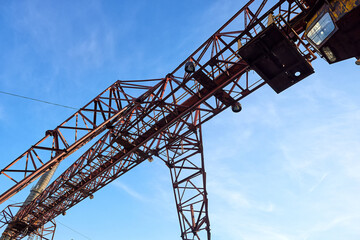 Steel gantry crane structure against blue sky, angular truss design with beams and joints. Used in...
