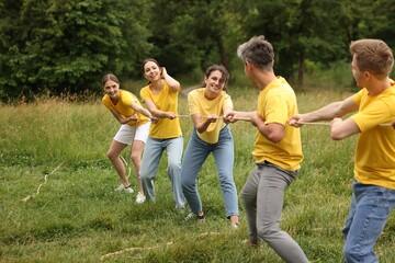Team building. Group of happy people playing tug of war with rope outdoors